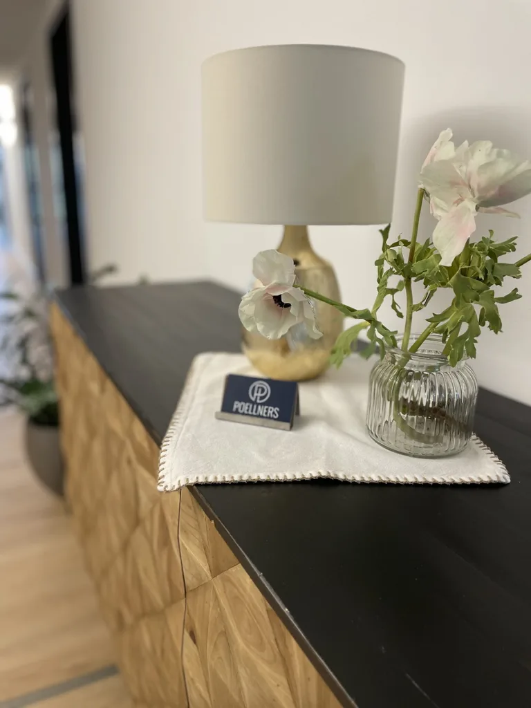 Nachttisch mit Lampe, Blumen und Gästeinformation im Hotelzimmer